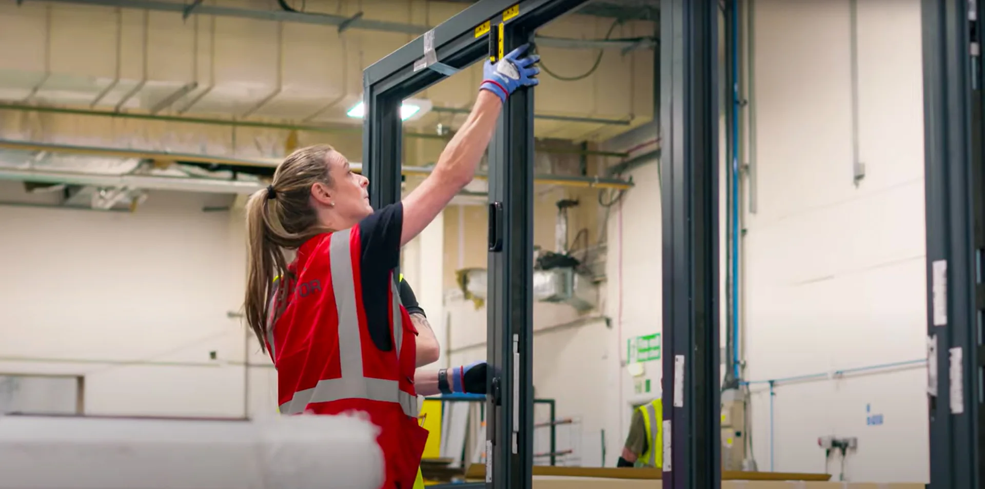 Close-up photo of a Made for Trade quality inspector meticulously examining the hinge on a finished Korniche bi-fold door frame. The inspector wears gloves and uses a screwdriver to check the hinge's alignment and tightness.