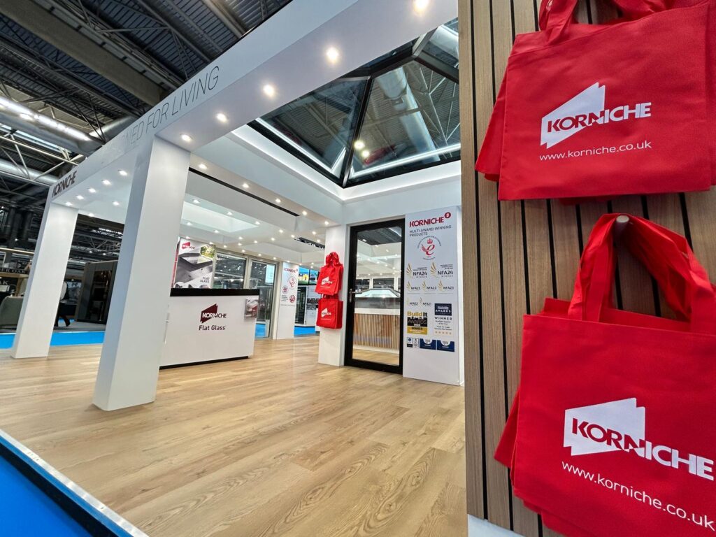 Red Korniche branded tote bags on stand walls, pre-show setup at the National Homebuilding & Renovating Show 2025.