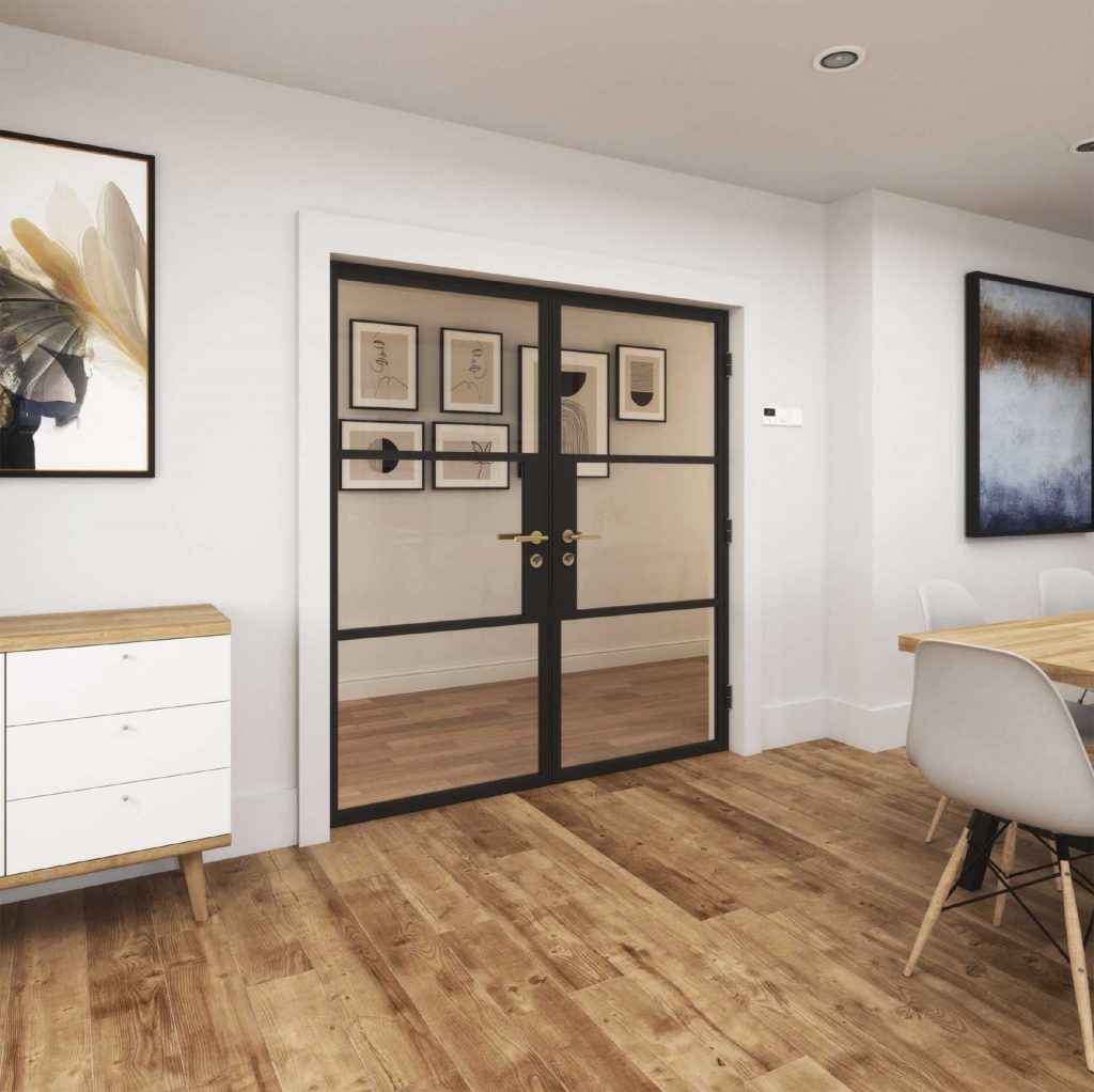 Korniche internal French doors with black frames and clear glass panels, forming a stylish partition between a dining area with a wooden table and chairs and another interior space in a home in Stockton-on-Tees, England. Artwork adorns the white walls surrounding the doorway.