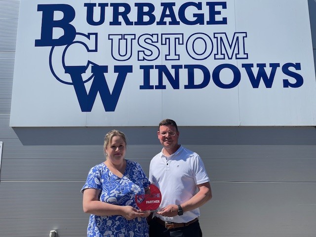 Katy Field, Customer Service Manager at Burbage Custom Windows, and Mike Robinson, Head of Sales & Operations at Made For Trade / Korniche, stand in front of the Burbage Custom Windows building holding an award, celebrating their new Premier Partner status.