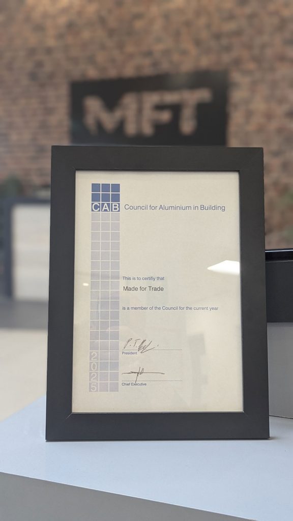 Framed CAB (Council For Aluminium In Building) certificate proudly displayed in the Made For Trade reception, with the large MFT logo visible in the background.