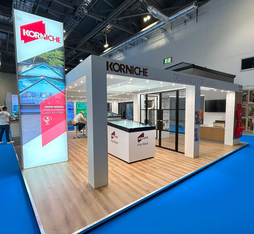 The full Korniche stand at a trade show, showcasing three innovative products: the slimline Roof Lantern, the elegant Flat Glass rooflight, and the modern Glass Partition system.