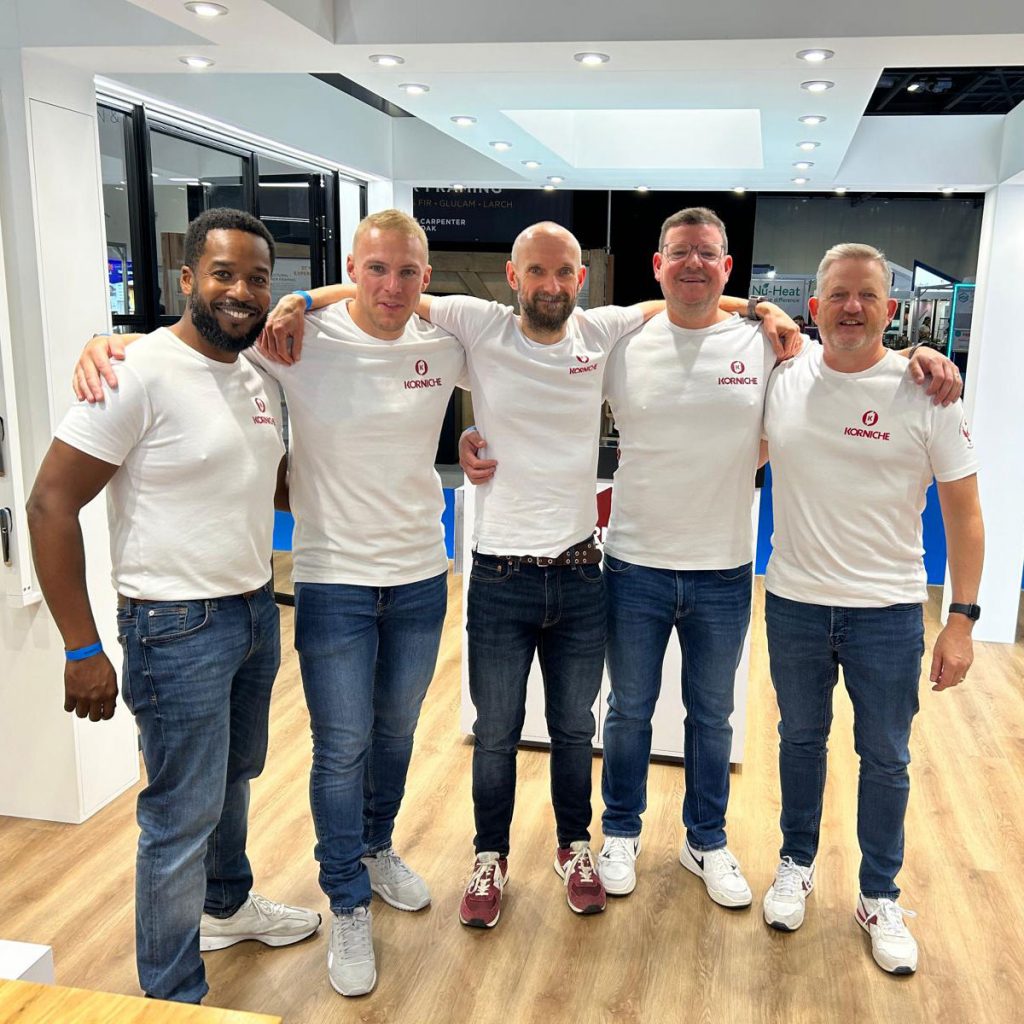 The Korniche team stands smiling on the exhibition stand at the Harrogate Homebuilding Show, wearing branded shirts and ready to talk to visitors.
